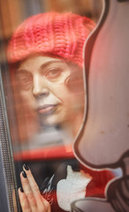 portrait of a woman in a knitting pink hat. she looks at us through the window