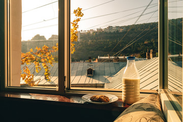 Breakfast set of a bottle of milk and cookies by the window in warm morning sunlight.