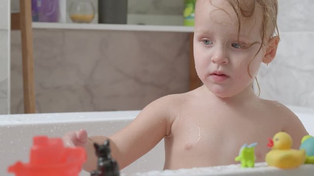 Funny two year old girl bathing and splashing water. Playful kid in the bath
