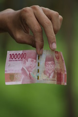 Hold 100,000 Indonesian Rupiahs with fingers. Money for legal payments in Indonesia