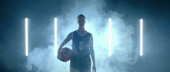 Caucasian female basketball player walking through the fog against bright lights, holding ball in her hands. 4K UHD 60 FPS SLOW MOTION shot on ARRI Alexa Mini with Atlas Orion 2x Anamorphic lens