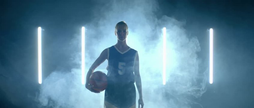 Caucasian female basketball player walking through the fog against bright lights, holding ball in her hands. 4K UHD 60 FPS SLOW MOTION shot on ARRI Alexa Mini with Atlas Orion 2x Anamorphic lens