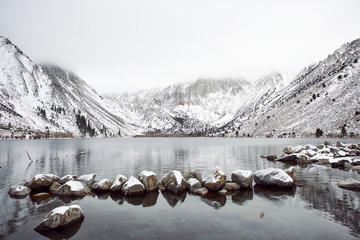 View of Lake on the Mountains in Winter Fog with Dramatic Snow Capped Mountains in the Background 
