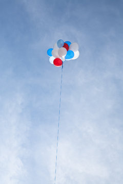 Red, white and blue balloons float high against a blue sky and hazy clouds.