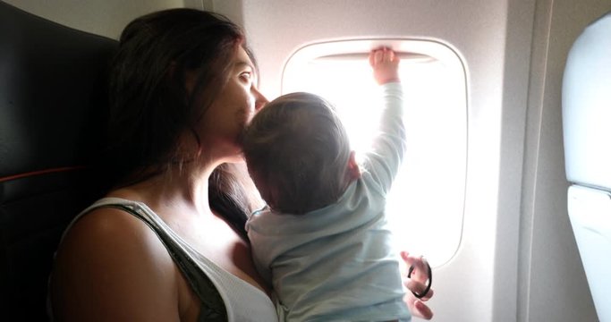 Baby reaching out to plane window. Mother traveling with infant son child