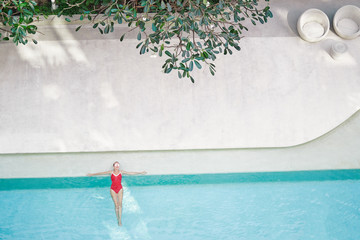 Fototapeta na wymiar Enjoying suntan. Vacation concept. Top view of slim young woman in red swimsuit in the swimming pool.