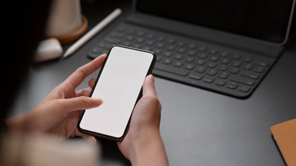 Cropped shot of a female typing blank screen smartphone on black desk