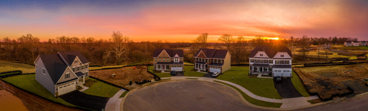 Aerial sunset view of a paved dead end street at a USA new construction American real estate site with some colonial luxury houses built around it and some lots are empty