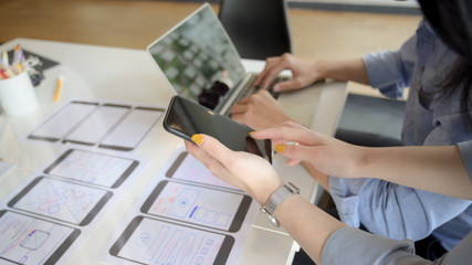 Close-up view of UI designer showing smartphone to her co-worker for the project