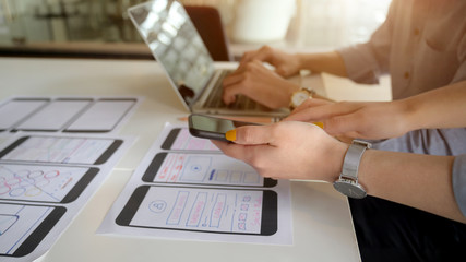 Close-up view of UI designer showing smartphone to her co-worker for the project