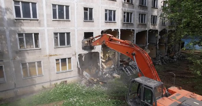 Excavator destructing the lower floors of old panel apartment house with following vertical flight over the building