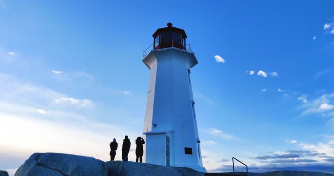 Peggy's Cove lighthouse with tourists standing beside, taking pictures and enjoying the view - Nova Scotia, Canada