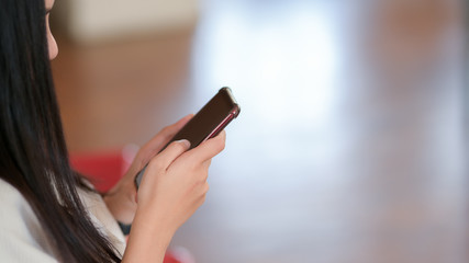 Side view of a girl using smartphone with blurred stylish living room background