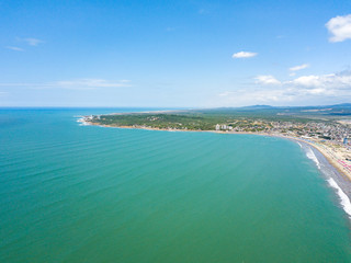 Fototapeta na wymiar Aerial drone view of the beach, tourists, sea and waves splashing in the coast of the town Playas General Villamil, Ecuador. Sunny day. Beach houses and the horizon with some clouds in background.