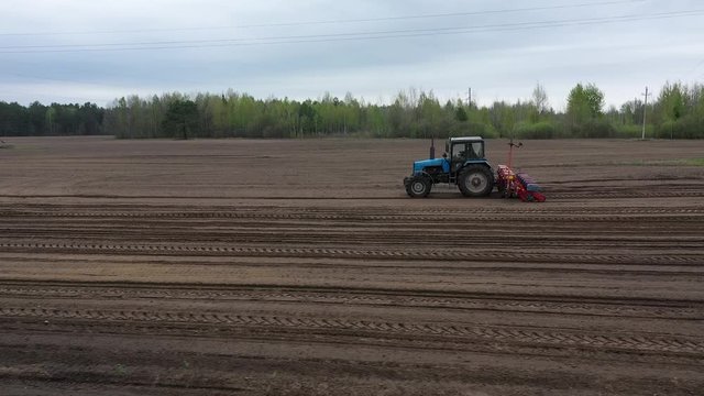 Aerial: Planting corn trailed planter in the field. Tactor with a seeder sows grain in the field. A farmer on a tractor with a seeder processes the field. 