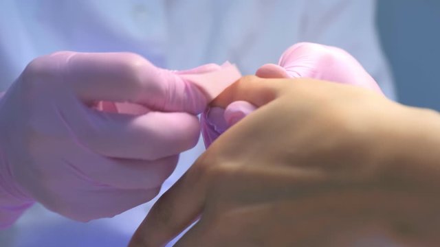 Manicurist master in gloves wipes nails with lint-free wipes after polymerization in UV lamp, closeup hands. Making manicure and shellac cover to nails, Hand hygiene and care, beauty industry concept.