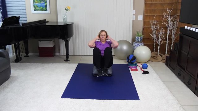 Middle-aged women doing v-sit crunches at home in living room gym.