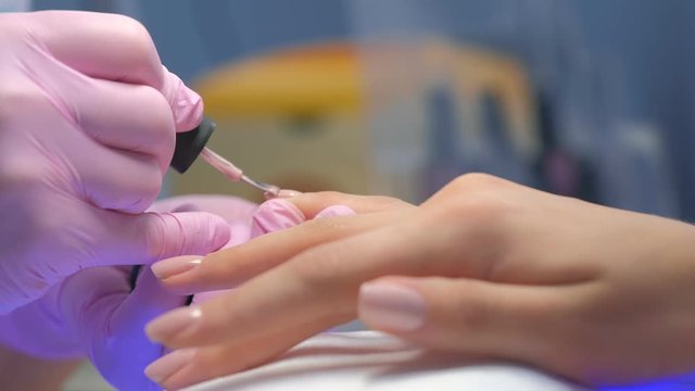 Manicurist master is covering painting client's nails shellac, hands closeup. Professional manicure in beauty salon. Hygiene and care for hands. Beauty industry concept.