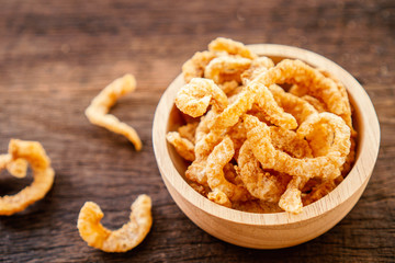 pork snack, rind, scratching or pork crackling in bowl on wooden table 