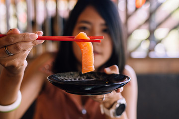 Hand woman using chopstick with raw salmon fillet on dish in restaurant,Japanese food