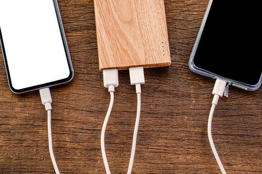 Tech Device Charge Sharing Concept With Smart Phone Charging With Power Bank On Wooden Table 