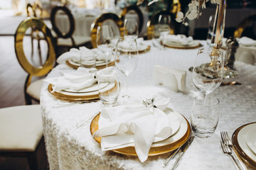 festive banquet tables are decorated with compositions of flowers, candles and figures of golden birds, on the tables are plates, glasses, napkins and cutlery