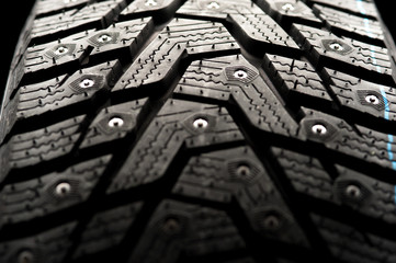 Studded car tire stands on a black background