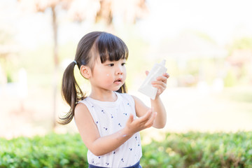 Adorable toddler girl putting solar cream on arms hands Smiling happy outdoors by pool under sunshine on beautiful summer day.Mixed race Asian / Caucasian kid girl.Sunscreen or sunblock and Skincare.