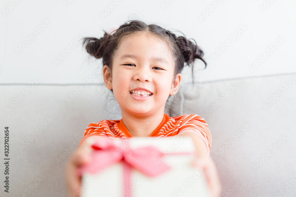 Wall mural Little asian girl smile and excited and holding red gift box on sofa in living room background.child holding gift box in Christmas and New year concept.