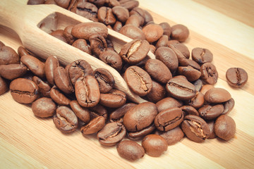 Heap of coffee grains with spoon on wooden board