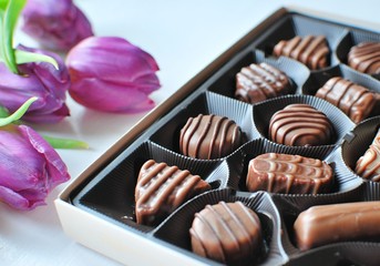 Chocolate candies in the box. Candy box and tulips for the romantic gift. Closeup view on white background.