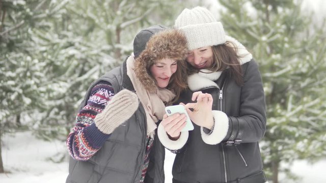 Women's Girlfriends watch photos on the phone taken on a walk in the winter forest