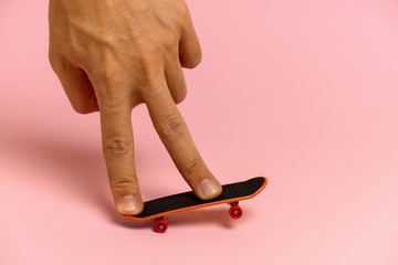 hand of a young man on a mini skateboard on a pink background