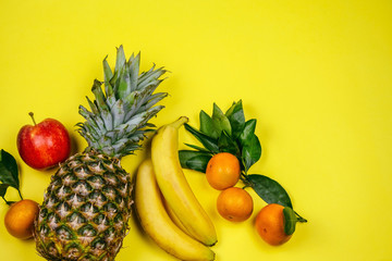 top view fresh tropical fruits layout pineapple,bananas, apple and tangerines on a yellow background