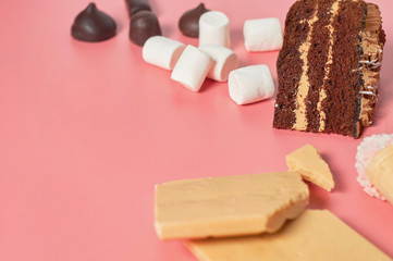 Pieces of chocolate cake near different sweets lies on pink table. Copy space