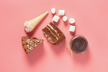 Pieces of chocolate cake near different sweets lies on pink table. Top view. Close-up