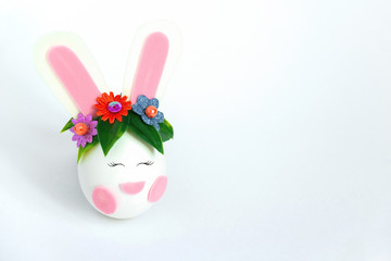 cute spring Easter card with an egg with bunny ears and a rim of spring flowers with copy space on a white background