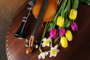 Violin with a bow, a bouquet of daffodils and tulips and clarinet on a wooden table.