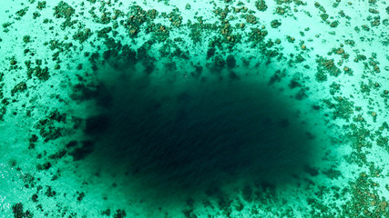 drone view of a dark blue hole in the ocean with beautiful coral reef around it in thailand