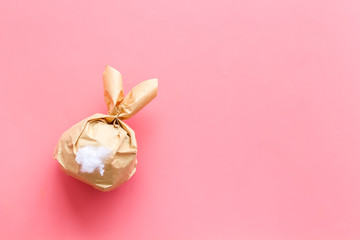 Easter gift in shape of bunny with tail on pink background top-down copy space