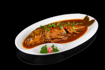 whole baked fish in spicy Chinese sauce on a black isolated background
