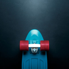 Skateboard with blue deck and red wheels on black background with copy-space top view. Concept of...