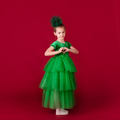 Beautiful little girl princess dancing in luxury green dress isolated on red background. Carnival party with costumes