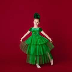 Beautiful little girl princess dancing in luxury green dress isolated on red background. Carnival party with costumes