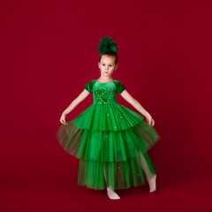 Beautiful little girl princess dancing in luxury green dress isolated on red background. Carnival...