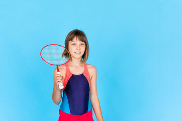 Young teenager girl jumping and playing badminton on blue background