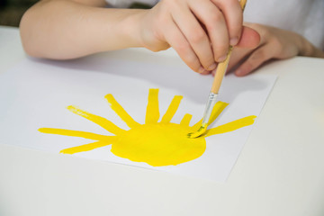 A child paints a yellow sun at a white table.