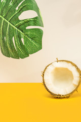 Half of fresh raw coconut  on yellow backgound with monstera leaf. Tropical food concept