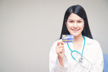 Beautiful Asian doctor holding a credit card standing smiling brightly White backdrop. Health service concept And finance in one card