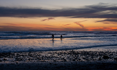 Fototapeta na wymiar Surfers on beach after Sunset